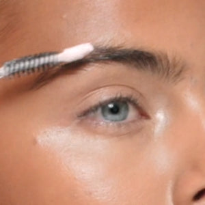 SWATI Cosmetics model applying tourmaline lash + brow booster serum on eyebrows.